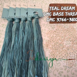May include: Teal Dream DMC base thread skeins with tags, displayed with a wooden block with text and a cream-colored doily. The thread is a blend of blue and green hues. The wooden block reads "TEAL DREAM DMC BASE THREAD DMC 3766-3810."