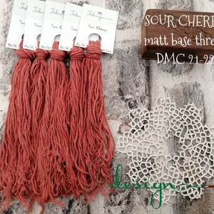 May include: Five spools of red-orange embroidery floss labeled "Sour Cherry" with the DMC color number 21-22. The floss is a matte base thread. A white crocheted doily is in the background.