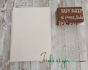 Peut inclure: Toile Aida crème de 16 points pour point de croix, avec le texte "Baby Sheep" et "DMC 3033-ecru" sur une boîte en bois. Un napperon en dentelle crème délicat et le mot "Judesign" sont également visibles.