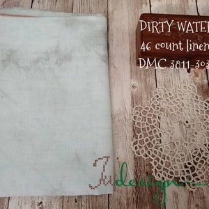 Puede incluir: Una tela de lino verde claro con un sutil patrón de mármol. La tela está etiquetada "Dirty Water 46 count linen DMC 3811-3032".
