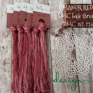 Può includere: Sei rocchetti di filo da ricamo DMC Manor Red, filo base DMC 152-223, con un pizzo all'uncinetto bianco su uno sfondo di legno.