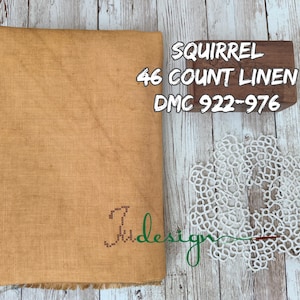 May include: A rectangular piece of golden-brown 46 count linen fabric with a visible weave, accompanied by a small wooden block labelled SQUIRREL 46 COUNT LINEN DMC 922-976 and a white circular lace doily with a needle and thread design.