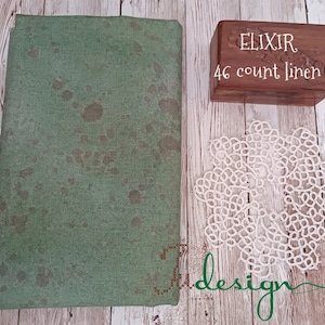 Puede incluir: Una tela de lino verde con manchas marrones. La tela está etiquetada como "ELIXIR 46 count linen".