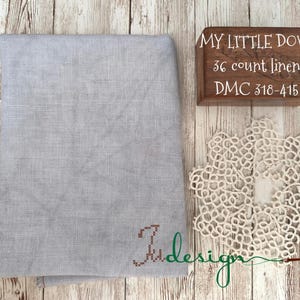 May include: A piece of light gray linen fabric with the text "My Little Dove" and "36 count linen" and "DMC 318-415" printed on a wooden box. The fabric is folded in half and has a small brown embroidered design in the lower right corner.