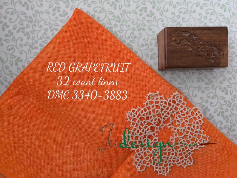 May include: An orange linen fabric square with the text "RED GRAPEFRUIT 32 count linen DMC 3340-3883". A small, carved wooden box and a white lace doily are also present. The background has a floral pattern.