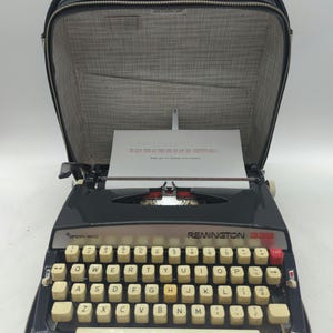 May include: A black Remington 333 portable typewriter with a white keyboard and a black carrying case. The typewriter has a red tab key and the words "Merry Rand" and "Remington 333" printed on the front.