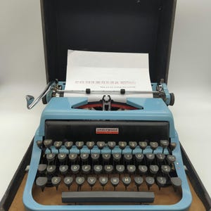 May include: A blue vintage Underwood typewriter in a black carrying case. The typewriter has a black and white keyboard with the letters QWERTYUIOPASDFGHJKLZXCVBNM.
