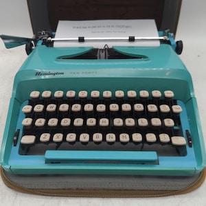 May include: A turquoise Remington Ten Forty typewriter with a QWERTY keyboard featuring white keys with black lettering. A sheet of paper is inserted into the carriage, and the machine is housed within a brown zippered carrying case base.