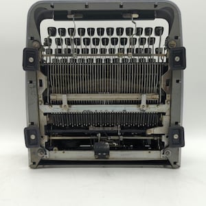 Pu&ograve; includere: Una macchina da scrivere vintage argentata con una tastiera nera e una cornice in metallo. La macchina da scrivere &egrave; aperta e i tasti sono visibili.