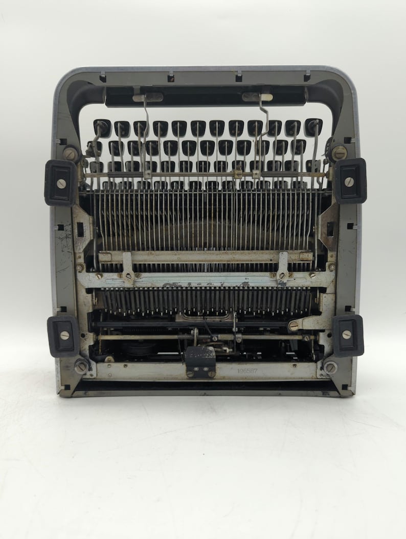 Pu&ograve; includere: Una macchina da scrivere vintage argentata con una tastiera nera e una cornice in metallo. La macchina da scrivere &egrave; aperta e i tasti sono visibili.