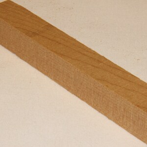 May include: A light brown wooden block with a square shape. The wood has a natural grain pattern.