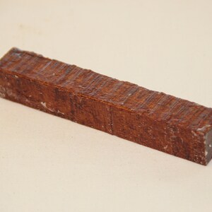 May include: A rectangular, brown wooden block with a textured surface. The wood grain is visible, and the block appears to be freshly cut. The block is approximately 1.5 inches wide and 6 inches long. The block is likely for woodworking or crafting.