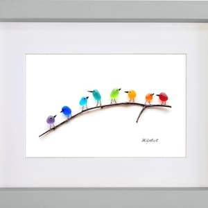May include: A framed art print featuring a row of colorful, glass-like birds perched on a brown branch. The birds are in shades of purple, blue, teal, green, yellow, orange, and red. The artwork is set against a white background and framed in a gray frame.