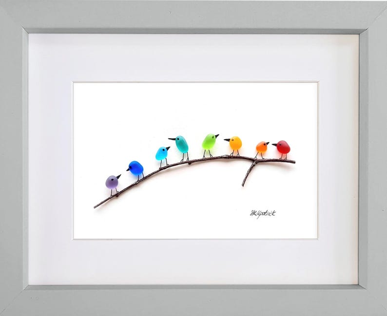 May include: A framed art print featuring a row of colorful, glass-like birds perched on a brown branch. The birds are in shades of purple, blue, teal, green, yellow, orange, and red. The artwork is set against a white background and framed in a gray frame.