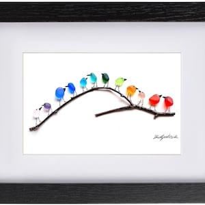 May include: A framed art piece featuring a branch with colorful glass birds. The birds are in shades of blue, green, orange, red, and purple. The artwork is set against a white background and framed in black.