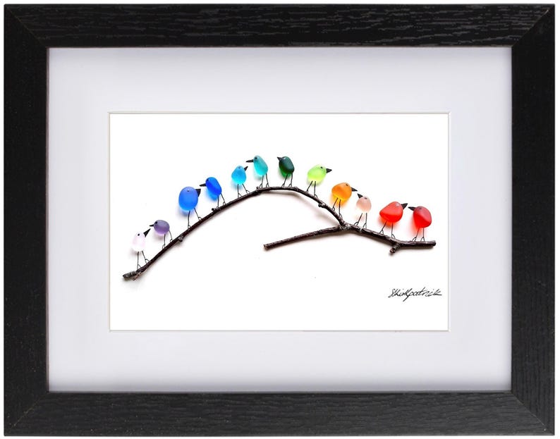 May include: A framed art piece featuring a branch with colorful glass birds. The birds are in shades of blue, green, orange, red, and purple. The artwork is set against a white background and framed in black.