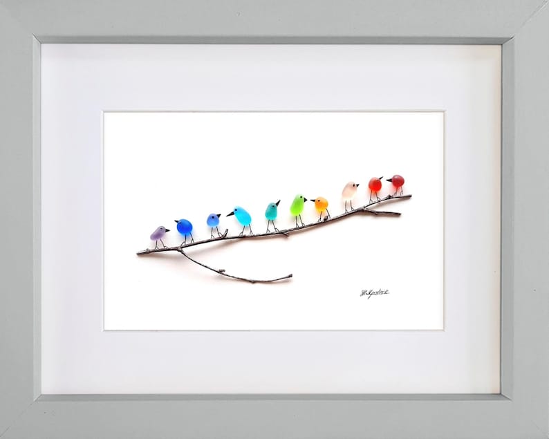 May include: A framed art print featuring a row of colorful glass birds perched on a brown branch. The birds are in shades of purple, blue, green, orange, and red. The artwork is set against a white background.