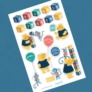 May include: A set of colourful stickers featuring animals, numbers, and phrases in French and English. The stickers include a hippopotamus, a monkey, and a bear. The numbers are displayed on blocks and a stack of blocks. The phrases include "Hurray", "Hi!", "Good morning Bonjour", "Youpi! er", and "Salut!"
