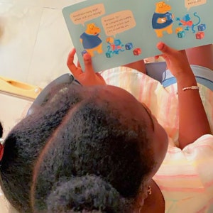 May include: A young girl is reading a children's book with colourful illustrations of animals and blocks. The book has the text "Good morning kids! What are you doing?" and "Bonjour Zo! Je compte les cubes, mais je crois que j'en ai perdu un".