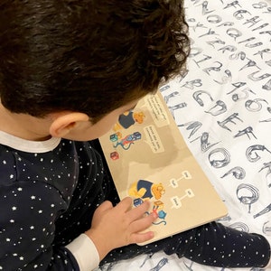 May include: A child is reading a book with colourful illustrations and text in English and French. The book features a cartoon character counting blocks. The text reads "If we count the numbers together?" and "Bonne id&eacute;e. Allez, commence par un."