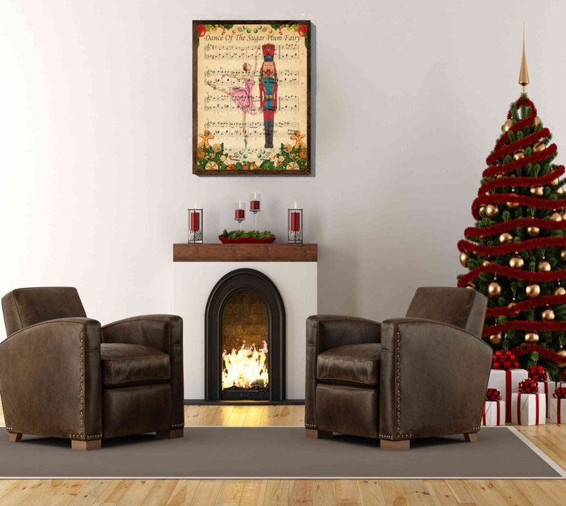 May include: A vintage-style Christmas print featuring a ballerina dancing with a Nutcracker soldier. The print is framed and hanging on a white wall above a fireplace with a lit fire. Two brown leather armchairs are positioned in front of the fireplace, and a decorated Christmas tree is in the background.