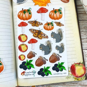 Puede incluir: Una hoja de pegatinas con tem&aacute;tica oto&ntilde;al con calabazas, setas, ardillas, bellotas, moras y polillas. Las pegatinas est&aacute;n sobre un fondo blanco y tienen un aspecto pintado a mano. El texto "autumunity 002" est&aacute; impreso en la esquina inferior derecha.