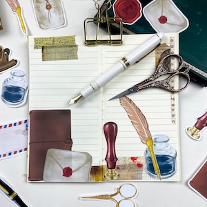 May include: An open notebook with lined pages, decorated with various stickers and paper ephemera. The stickers include a brown leather journal, a quill pen, a bottle of ink, a wax seal, and a pair of scissors. The notebook is on a white surface.