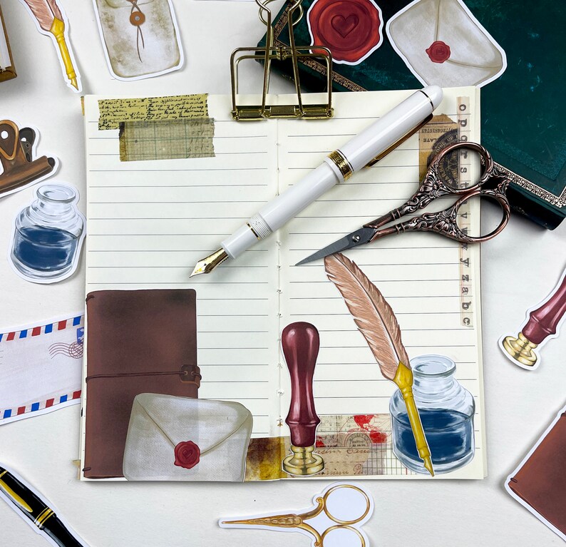 May include: An open notebook with lined pages, decorated with various stickers and paper ephemera. The stickers include a brown leather journal, a quill pen, a bottle of ink, a wax seal, and a pair of scissors. The notebook is on a white surface.