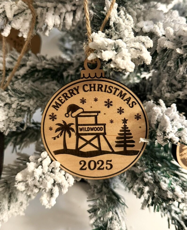 Puede incluir: Adorno navide&ntilde;o circular de madera con la inscripci&oacute;n "Merry Christmas" y el a&ntilde;o "2025". El dise&ntilde;o incluye un puesto de salvavidas, una palmera, un &aacute;rbol de Navidad, copos de nieve y un gorro de Pap&aacute; Noel.