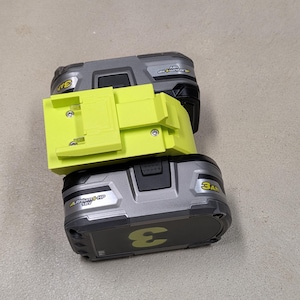 K&ouml;nnte beinhalten: Ein gr&uuml;ner und grauer Batterieadapter f&uuml;r ein Elektrowerkzeug. Der Adapter ist mit "Lithium HP 18V" und "3Ah" beschriftet.