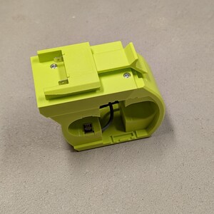 K&ouml;nnte beinhalten: Ein limegr&uuml;ner Kunststoff-Batterieladeger&auml;t mit einem schwarzen Kabel. Das Ladeger&auml;t hat einen Steckplatz f&uuml;r eine Batterie und eine kleine rechteckige &Ouml;ffnung an der Seite.