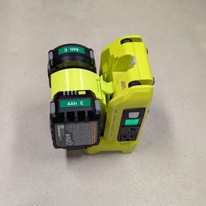K&ouml;nnte beinhalten: Ein gelber und schwarzer Stromwandler mit zwei angeschlossenen 4Ah E-Batterien. Der Wechselrichter hat eine Leistung von 300 Watt und einen gr&uuml;nen Einschaltknopf.