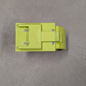 K&ouml;nnte beinhalten: Ein limegr&uuml;nes, 3D-gedrucktes Kunststoffteil mit rechteckiger Form und einem kleinen Griff. Das Teil hat mehrere kleine L&ouml;cher und einen Schlitz oben.