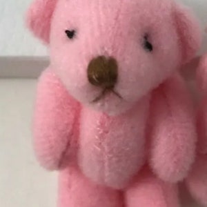 May include: A small, pink teddy bear with a brown nose and black eyes. The bear is made of a soft, plush material and has stitched details. The image includes the text "Select larger area."