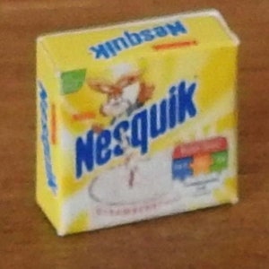 Puede incluir: Caja amarilla con el logotipo de Nesquik y un conejo de dibujos animados en la parte delantera. La caja dice "Nesquik" en letras azules y "Chocolate bebible" en letras más pequeñas.