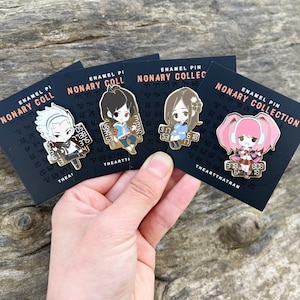 Puede incluir: Cuatro pines de esmalte con personajes de anime de la serie Nonary Games. Cada pin tiene un fondo negro con texto blanco que dice "Nonary Collection" y un borde dorado. Los personajes están representados en estilo chibi y visten diferentes atuendos. Los pines se sostienen en una mano.