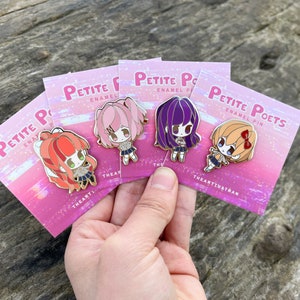Puede incluir: Cuatro pines de esmalte con personajes de estilo anime con cabello rosa, morado, naranja y rojo. Los pines están en tarjetas con el texto "Petite Poets Enamel Pin" y el nombre del artista "TheArtThatRan".