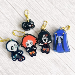 May include: Five colorful acrylic keychains with gold-colored chain attachments. The keychains feature cartoon characters in various poses and outfits. The characters include a black cat, a skeleton, and three girls with different hair colors and outfits.