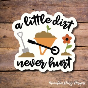 May include: A white sticker with a black and white illustration of a wheelbarrow, shovel, and flower. The text "a little dirt never hurt" is written in black cursive.
