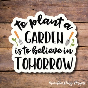 May include: White sticker with black text that reads "To plant a garden is to believe in tomorrow". The sticker features a small green plant and a gardening fork on the left and a small green plant and a gardening trowel on the right.