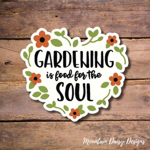 May include: A white heart-shaped sticker with green leaves and orange flowers around the edges. The text "GARDENING is food for the SOUL" is written in black.