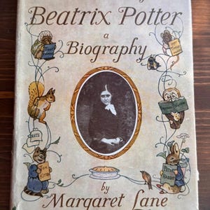 Puede incluir: Un libro de tapa dura titulado The Tale of Beatrix Potter a Biography de Margaret Lane. La cubierta de color blanco roto presenta un retrato ovalado central de Beatrix Potter rodeado de ilustraciones de personajes como Peter Rabbit y Tom Kitten.