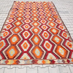 May include: A traditional Turkish rug with a geometric pattern in shades of red, orange, yellow, and blue. The rug has a fringe border and is made of wool.