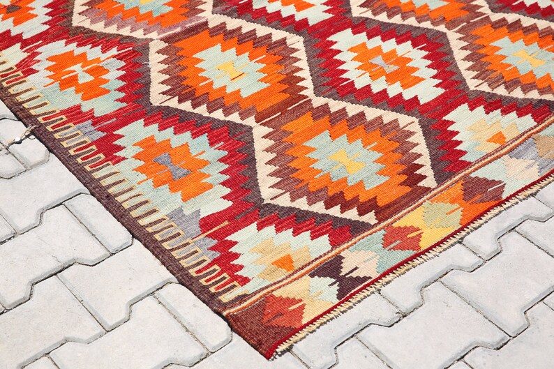 May include: A colorful, geometric patterned rug with red, orange, brown, and white colors. The rug is made of wool and has a traditional design.