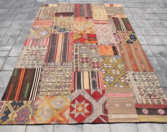 May include: A large, rectangular patchwork rug with a variety of geometric and striped patterns in shades of red, brown, beige, and blue. The rug is made up of numerous rectangular pieces sewn together.