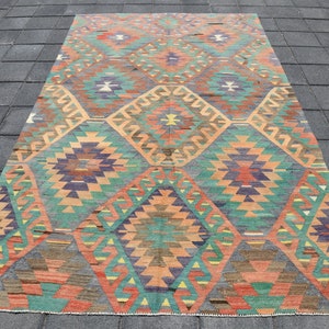 Pu&ograve; includere: Un tappeto turco vintage con un motivo geometrico in tonalit&agrave; di arancione, verde, blu e marrone. Il tappeto ha un aspetto sbiadito e usurato, che gli conferisce un carattere unico.