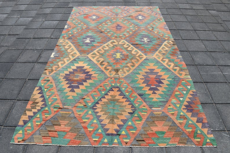 Pu&ograve; includere: Un tappeto turco vintage con un motivo geometrico in tonalit&agrave; di arancione, verde, blu e marrone. Il tappeto ha un aspetto sbiadito e usurato, che gli conferisce un carattere unico.