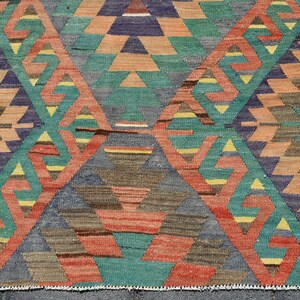 Pu&ograve; includere: Un tappeto colorato con un motivo geometrico in tonalit&agrave; di rosso, arancione, verde, blu e marrone. Il tappeto ha un bordo con frange.