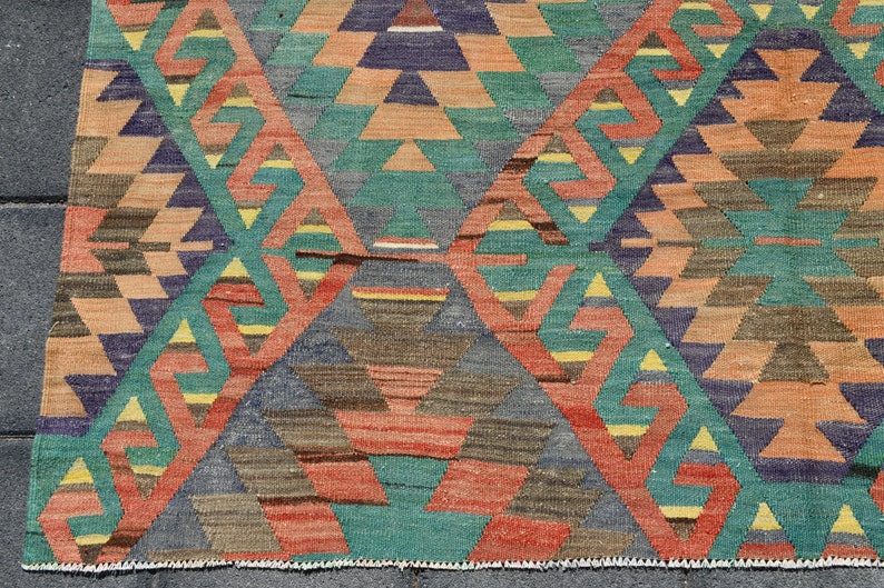 Pu&ograve; includere: Un tappeto colorato con un motivo geometrico in tonalit&agrave; di rosso, arancione, verde, blu e marrone. Il tappeto ha un bordo con frange.