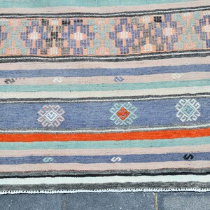 May include: A handwoven rug with a striped pattern in shades of blue, orange, pink, and green. The rug has a fringe border.